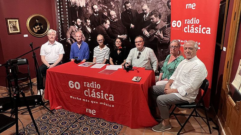 Celebración del 60 aniversario de Radio Clásica de RNE en un museo, con 7 personas alrededor de una mesa y arte de guitarras de fondo.