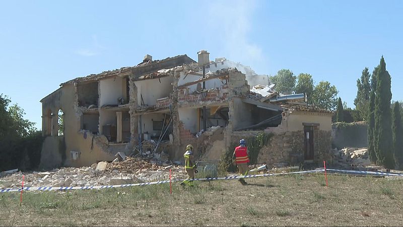 Edifici rural en ruines amb tejat col·lapsat i parets derruïdes. Bombers amb cascos i uniformes d'emergència s'acosten a la zona acordonada per avaluar els danys.