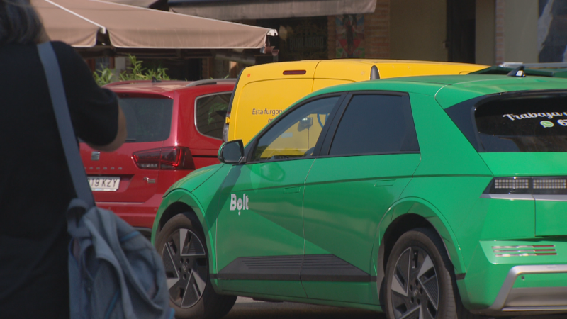 Vehículo Bolt verde brillante con logo amarillo en Pamplona. Ventanilla trasera con texto parcial "Trabaja y...", icono de WhatsApp y "6". Detrás, SUV rojo "19 KZY" y furgoneta amarilla.