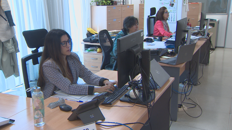 Oficina moderna con tres mujeres trabajando frente a sus ordenadores. Una de ellas, con gafas y chaqueta de cuadros, usa un teclado y una tablet con logo Cisco.