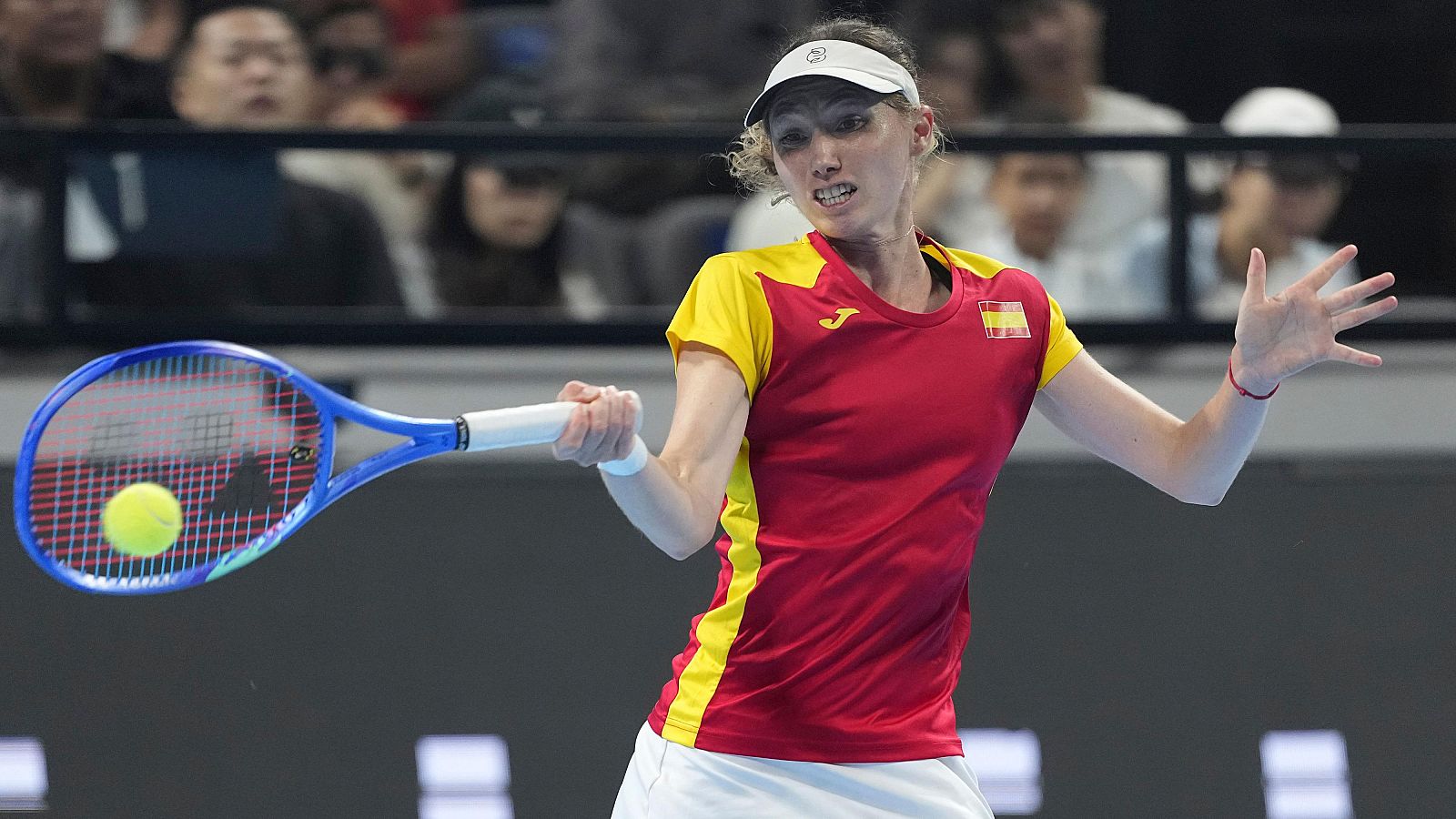 Sara Sorribes Tormo, tenista española, golpea una pelota de tenis durante un partido. Lleva el uniforme de España y su expresión es de máxima concentración.