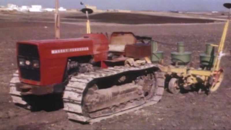 Tractor Massey Ferguson rojo de orugas con sembradora amarilla de tolvas verdes en campo labrado.