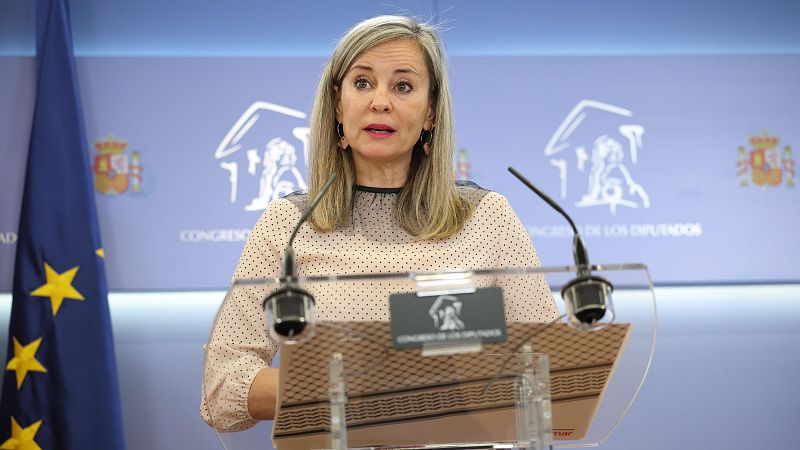 Verónica Barbero, periodista, habla en el Congreso de los Diputados, con las banderas de la UE y España al fondo y el emblema del Congreso en el atril.