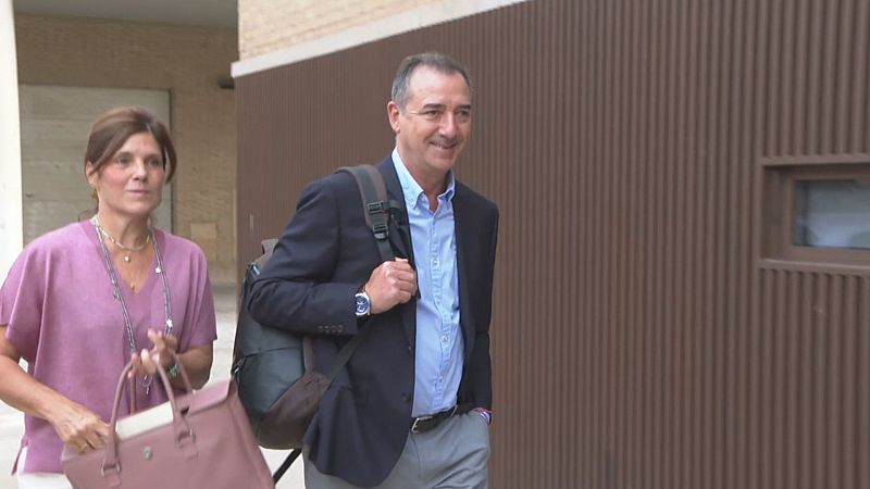Robert Raga, alcalde de Riba-roja de Túria, camina con una mujer frente a un edificio marrón. Él viste camisa azul y americana, ella blusa malva y collares.