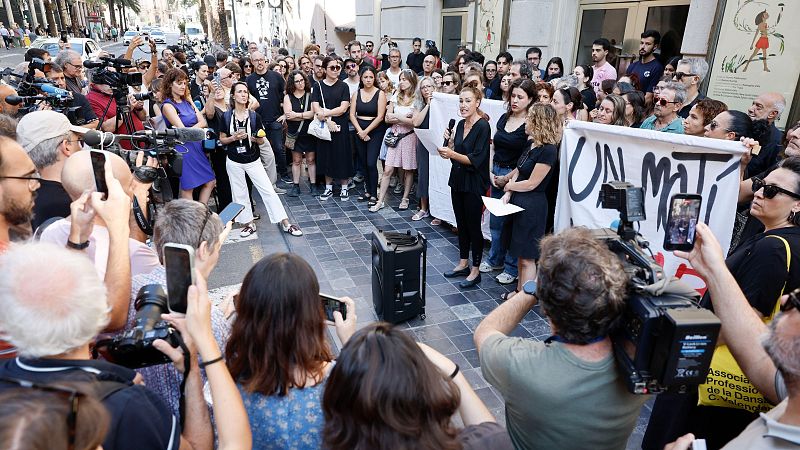 Oradora con micrófono frente a multitud y medios, pancarta "UN MATÍ" y logo de la Asociación Profesional de la Danza C. Valenciana.