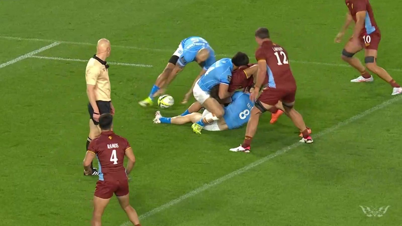 Jugadores de rugby en disputa por el balón en el suelo, con un árbitro observando. Equipaciones azul claro y granate, césped verde y balón amarillo.