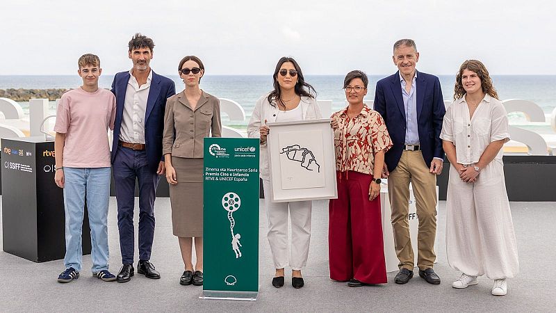 Siete personas posan frente a las letras "SSIFF" y el mar. Antonio de la Torre está presente. Un banner con logotipos de UNICEF y RTVE, y textos en euskera y español, se ve en la imagen.