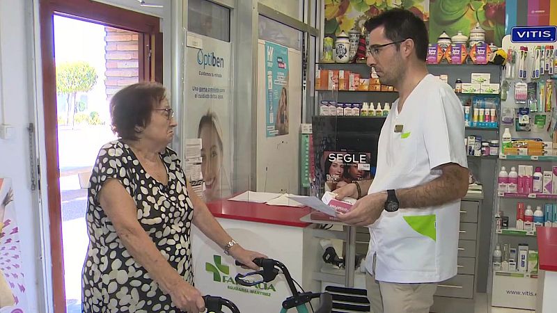 Farmacia Isabel Martínez: mujer mayor con andador y farmacéutico con uniforme blanco y caja rosa interactúan.