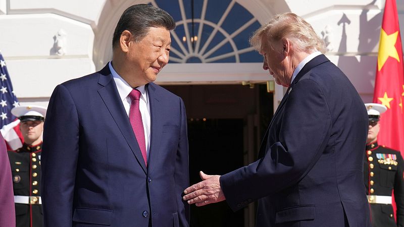 Xi Jinping y Donald Trump se saludan frente a la Casa Blanca, con las banderas de China y EE.UU. al fondo. Ambos visten trajes formales.