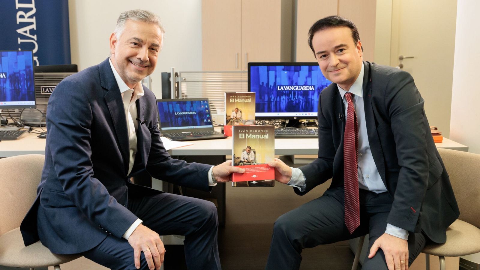 Jordi Basté e Iván Redondo presentan el libro "El Manual" de Redondo en un estudio de La Vanguardia. Ambos sonríen a cámara, con copias del libro y logotipos del periódico de fondo.