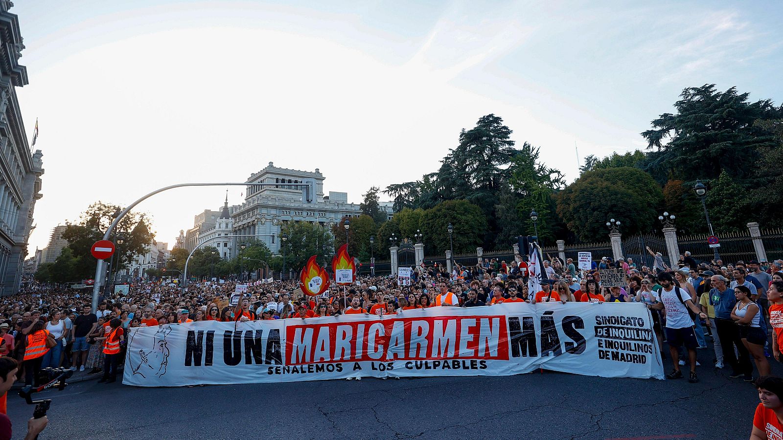 Manifestación masiva en Madrid convocada por el Sindicato de Inquilinos e Inquilinas bajo la pancarta "NI UNA MARICARMEN MÁS". Se observan edificios clásicos y modernos, árboles y mobiliario urbano.