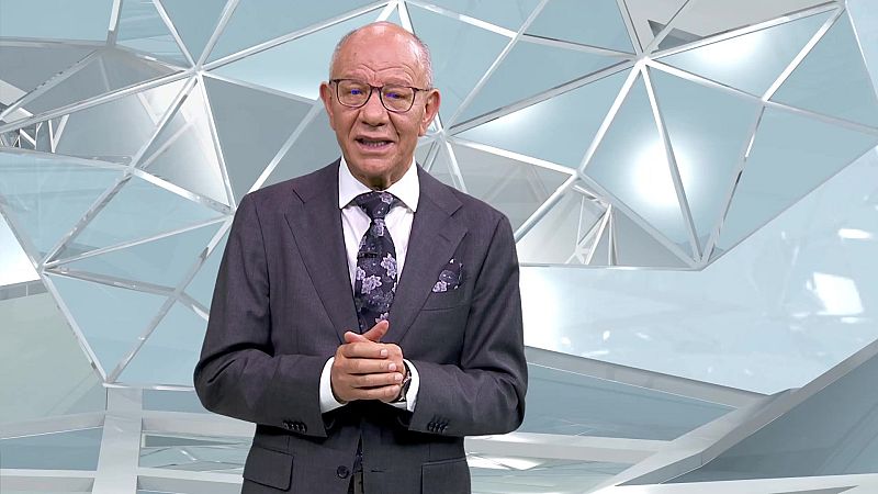 Fernando Medina, presentador de TVE, posa con traje gris, camisa blanca y corbata floral en un set de televisión con fondo geométrico azul y blanco.