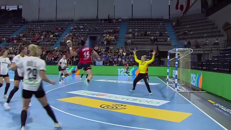 Jugadora de balonmano con dorsal 15 en rojo salta para lanzar. Portera de amarillo se prepara. En primer plano, jugadora con dorsal 29 y "ADUL".