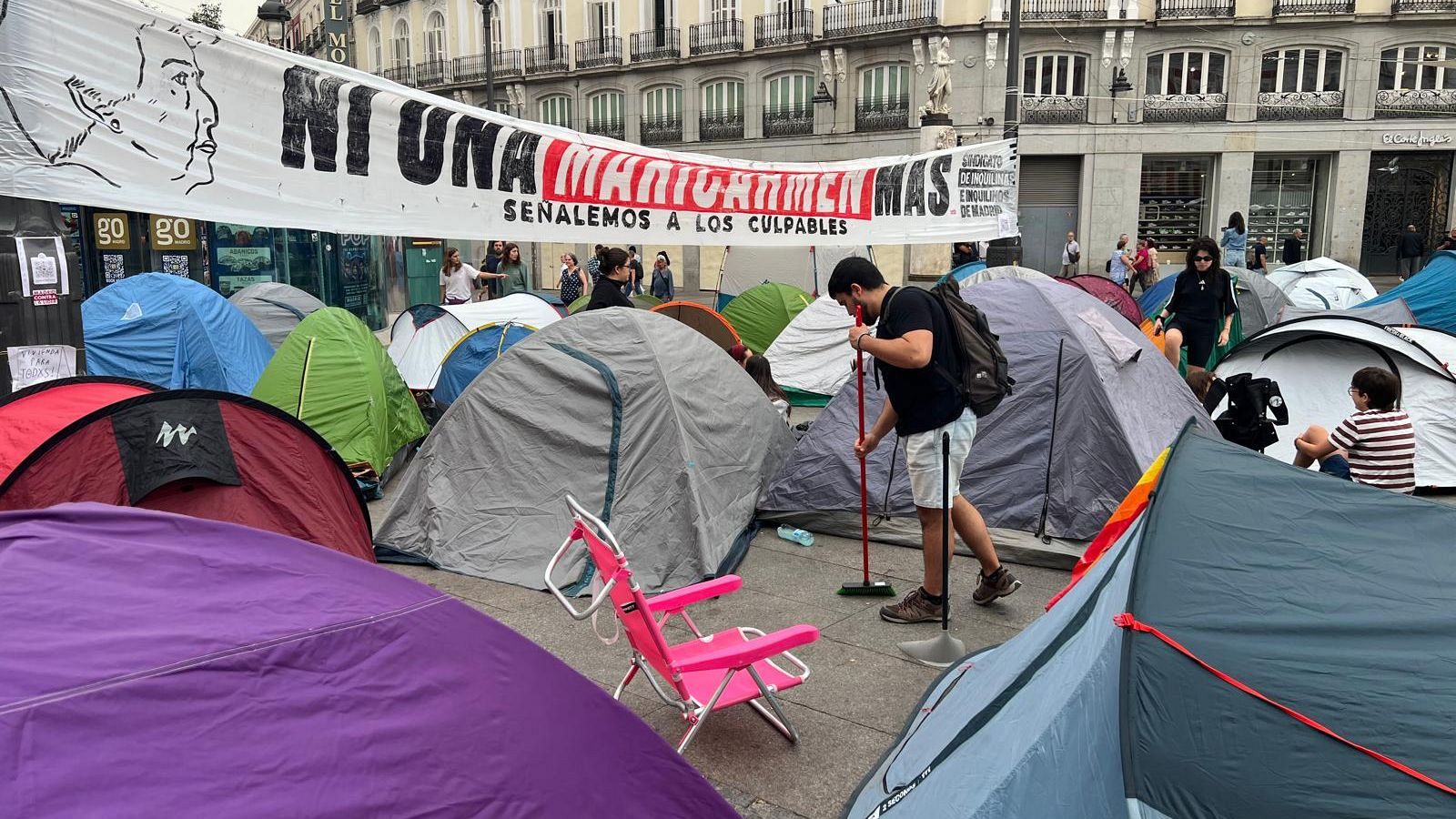 Un joven limpia alrededor de su tienda de campaña, en la Puerta del Sol de Madrid.