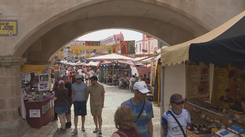 Mercado artesanal en la Plaza de San José, con puestos de miel, conservas y jabones bajo un arco de piedra y decoraciones andalusíes. Multitud de gente disfruta del evento.