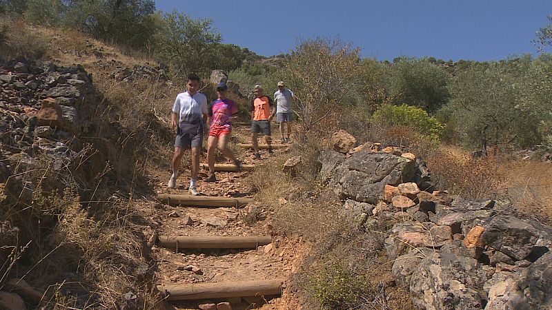 Cuatro senderistas con ropa deportiva descienden por un sendero escalonado de tierra durante la Ruta Peñas Blancas en La Zarza, Extremadura.
