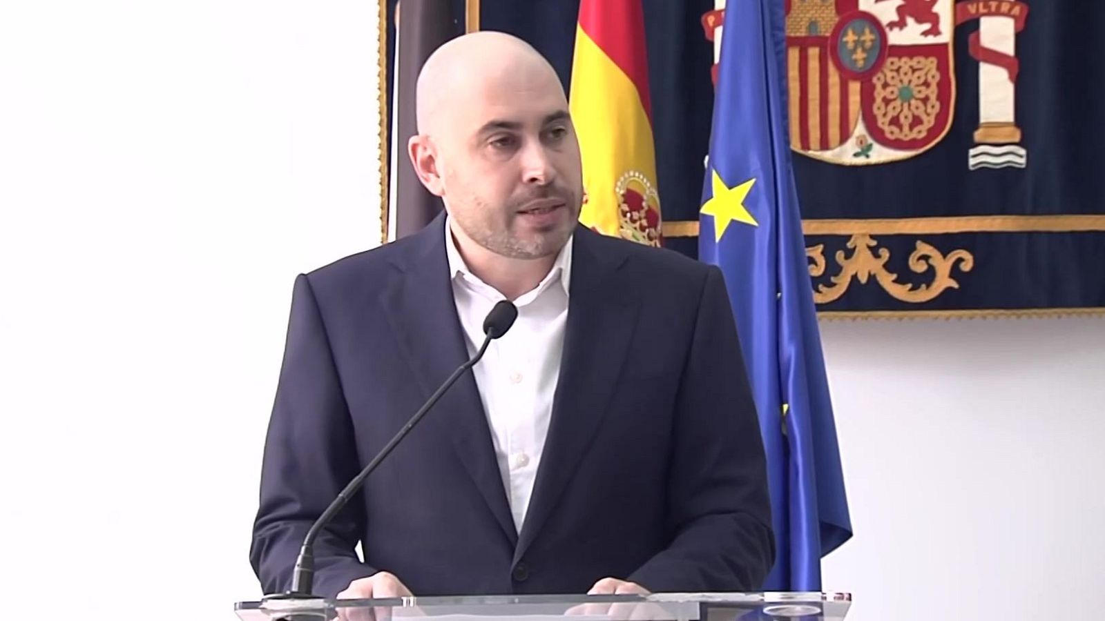 Salvador Ismael Mateos Pérez, ex Delegado del Gobierno en Ceuta, habla en un acto oficial con las banderas de España y la UE de fondo.