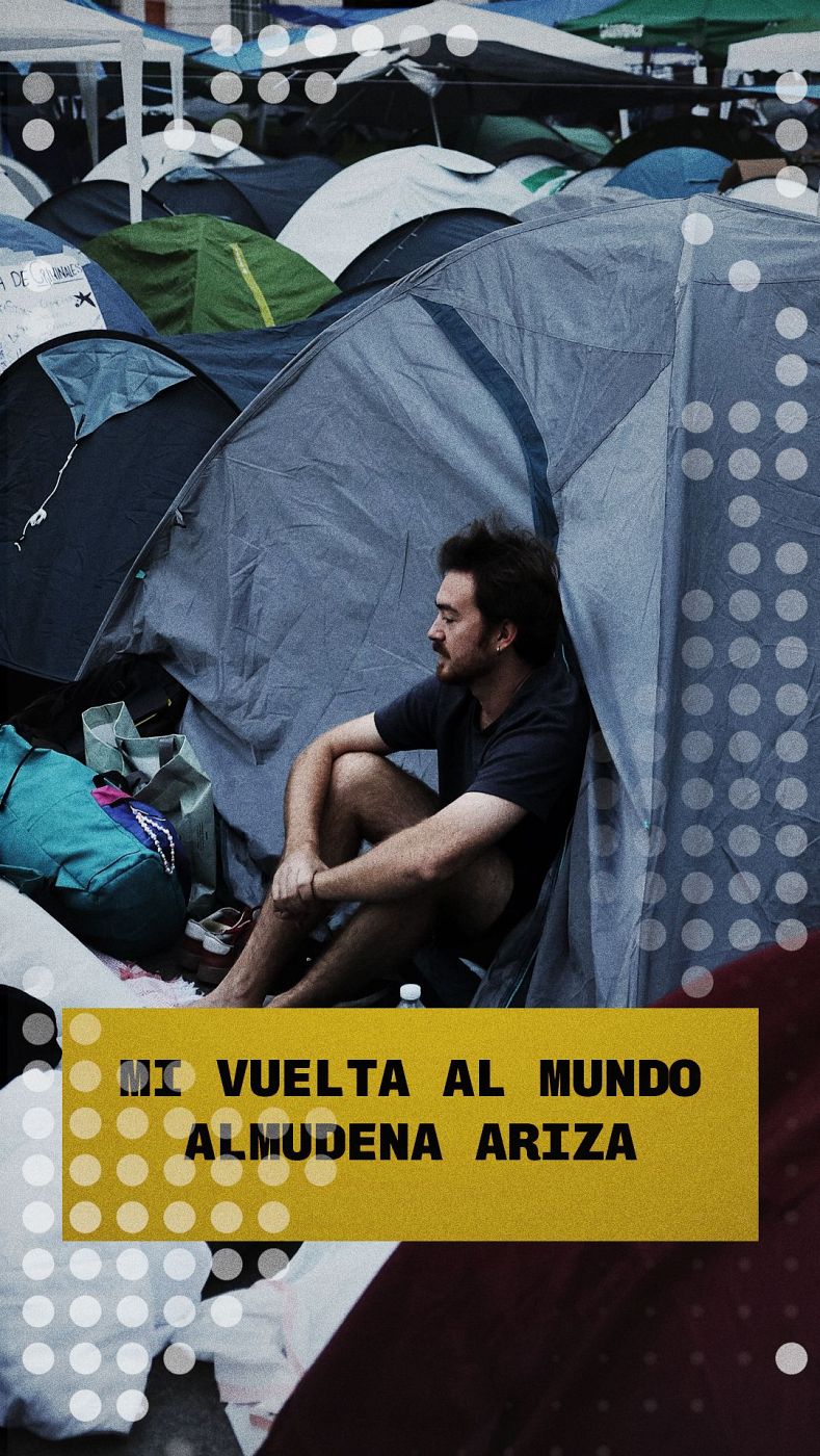 Hombre con barba y bigote sentado en tienda de campaña gris azulada, junto a mochila turquesa. Fondo de campamento con múltiples tiendas. Recuadro amarillo con texto 'MI VUELTA AL MUNDO ALMUDENA ARIZA'.