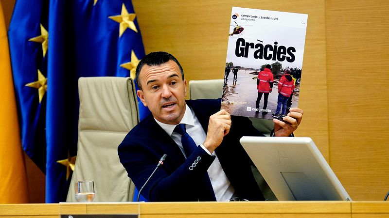 Joan Baldoví, político, sostiene un cartel de "Gràcies" de Compromís con imágenes de rescate en inundaciones y un helicóptero rojo.