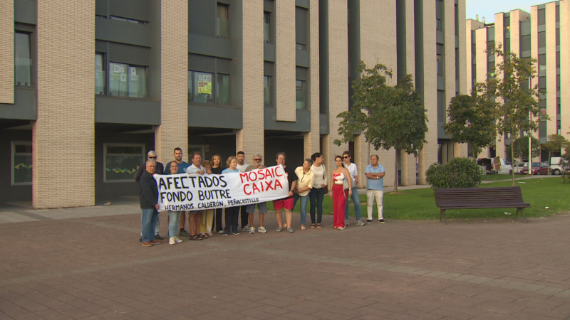 Vecinos de Peñacastillo protestan frente a sus pisos con una pancarta que dice 'AFECTADOS FONDO BUITRE MOSAIC CAIXA HERMANOS CALDERÓN'.