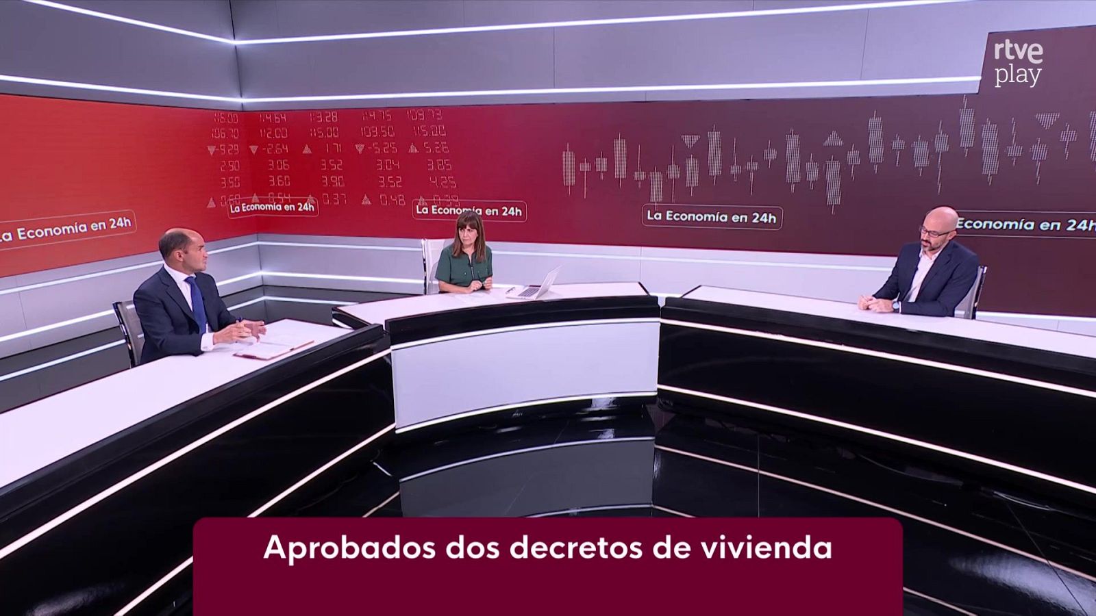 Tres personas debaten en el plató de 'La Economía en 24h' de RTVE, con gráficos financieros de fondo y el rótulo 'Aprobados dos decretos de vivienda'.