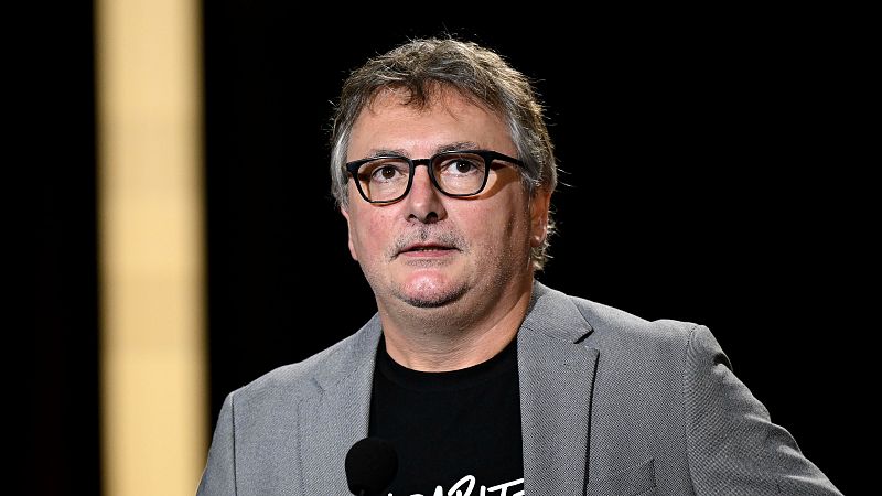 El periodista Xabier Fortes, con gafas de montura negra y chaqueta gris, habla frente a un micrófono en un plató de televisión con fondo oscuro.