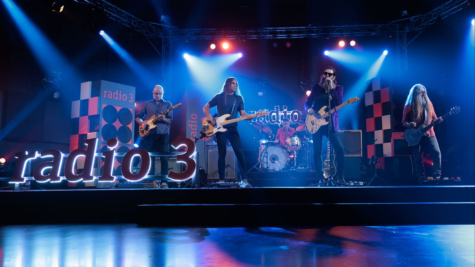 La banda Corizonas actúa en el escenario de 'Los conciertos de Radio 3', con un gran letrero luminoso en el suelo y focos azules iluminando a los músicos con sus guitarras.