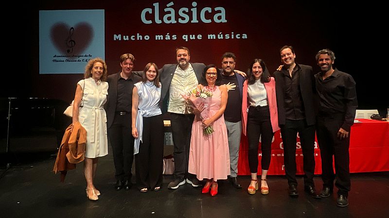 Nueve personas, incluido el periodista Martín Llade, posan en un escenario ante una pantalla roja con el logo de la Asociación de Amigos de la Música Clásica de Castilla-La Mancha.