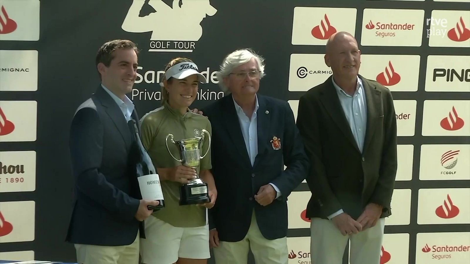 Mireia Prat posa con un trofeo junto a Gonzaga Escauriaza y otros dos hombres en la entrega de premios del Santander Golf Tour, frente a un panel de patrocinadores.