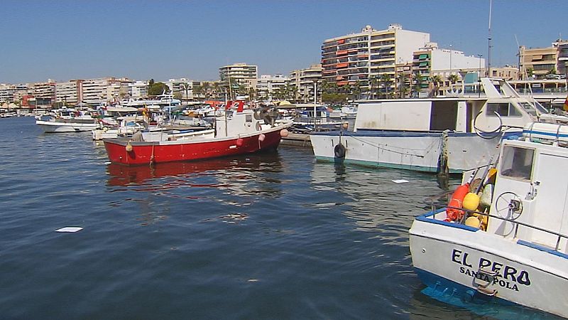 Embarcaciones amarradas en el puerto de Santa Pola, destacando en primer plano la popa de un barco blanco con el nombre "EL PERO" y de fondo el paseo marítimo bajo un cielo despejado.