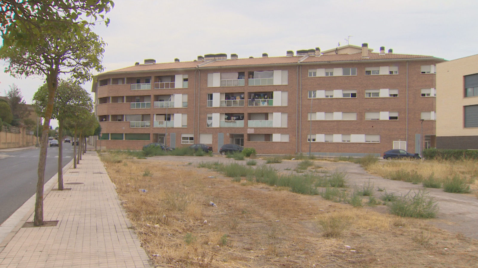 Edificio residencial de ladrillo visto de cuatro plantas en Cintruénigo, situado frente a un solar de tierra bajo un cielo nublado.