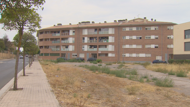 Edificio residencial de ladrillo visto de cuatro plantas en Cintruénigo, situado frente a un solar de tierra bajo un cielo nublado.