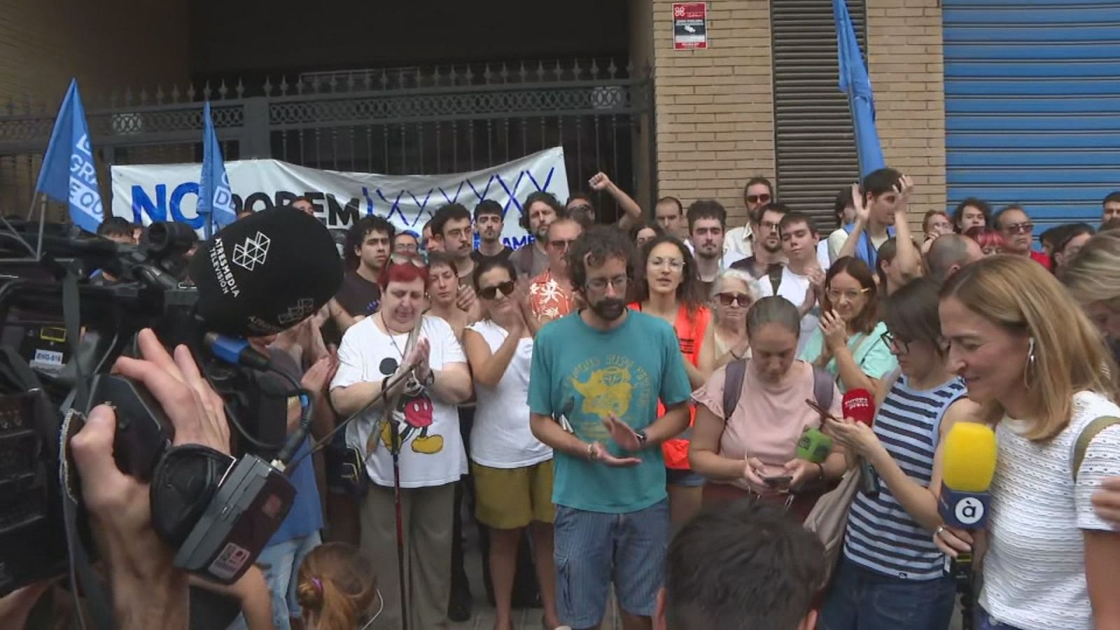 Portavoces de una protesta contra un desahucio en Burjassot atienden a micrófonos de À Punt y Atresmedia frente a una multitud con pancartas.