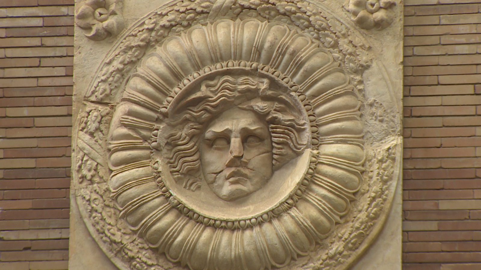 Relieve romano de piedra con el rostro de Medusa esculpido en un medallón circular, decorado con guirnaldas y expuesto sobre una pared de ladrillo en el Museo de Arte Romano de Mérida.