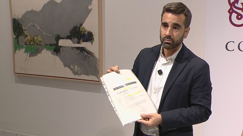 El concejal Borja Sanjuán sostiene un documento con texto resaltado en amarillo durante una comparecencia, vistiendo traje azul y camisa blanca ante un fondo con un cuadro abstracto.