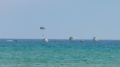 Un paracaidista militar desciende sobre el mar turquesa junto a lanchas de apoyo y otros paraca�das flotando en el agua durante unas maniobras del Ej�rcito del Aire.