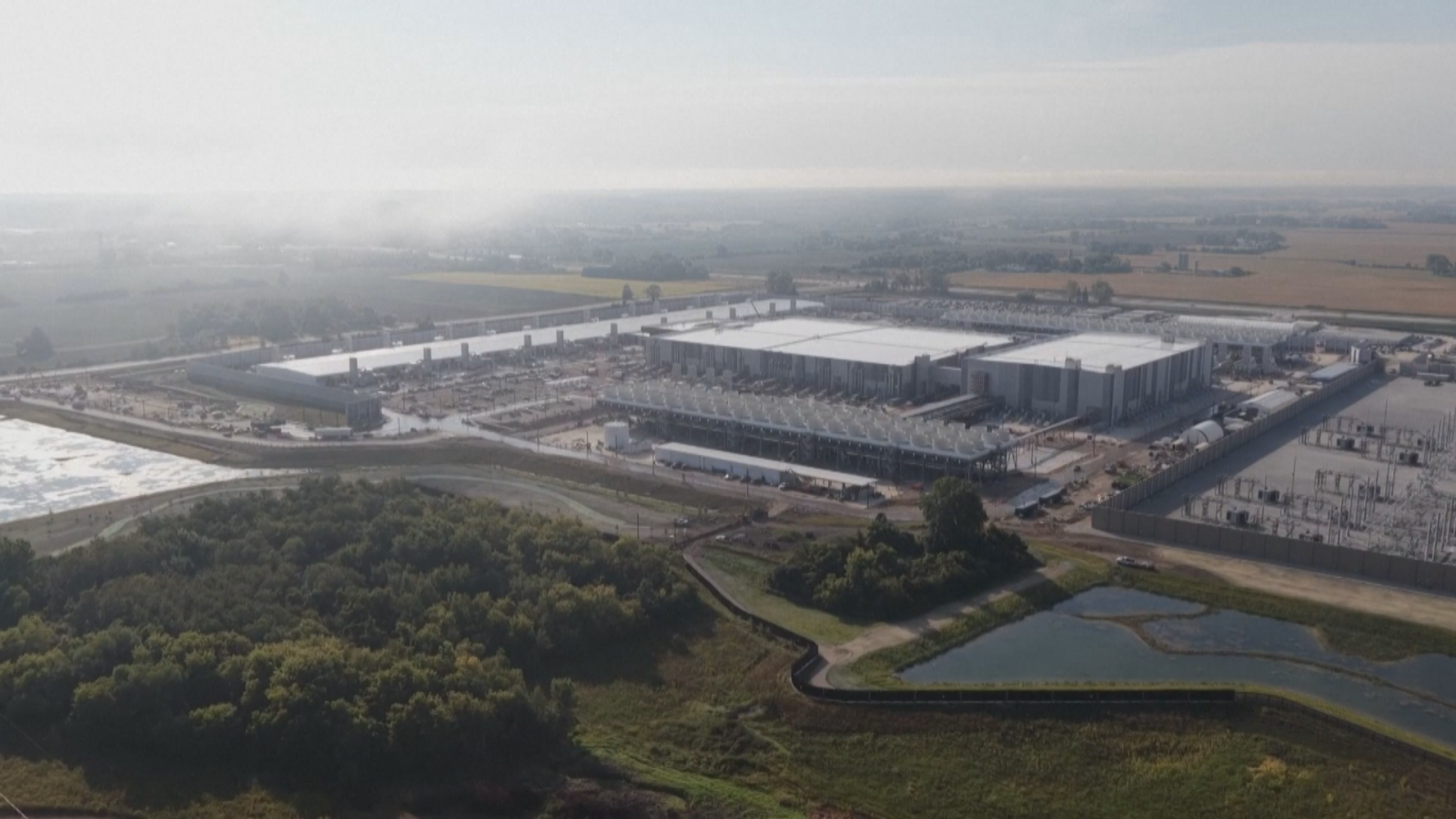 Vista aérea del centro de datos de AWS en Calatorao, Zaragoza, con grandes naves industriales de techos blancos, una subestación eléctrica y campos agrícolas al fondo.