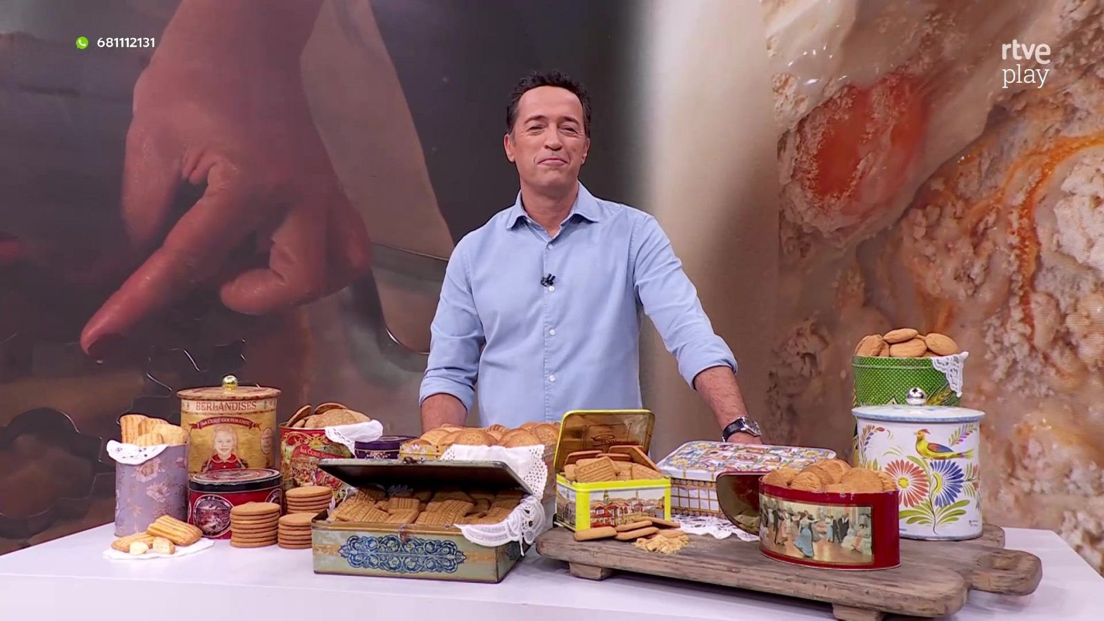 Jacob Petrus sonríe en el plató de "Aquí la Tierra" tras una mesa con botes de galletas vintage, bajo el logo de rtve play y el número de WhatsApp 681112131.