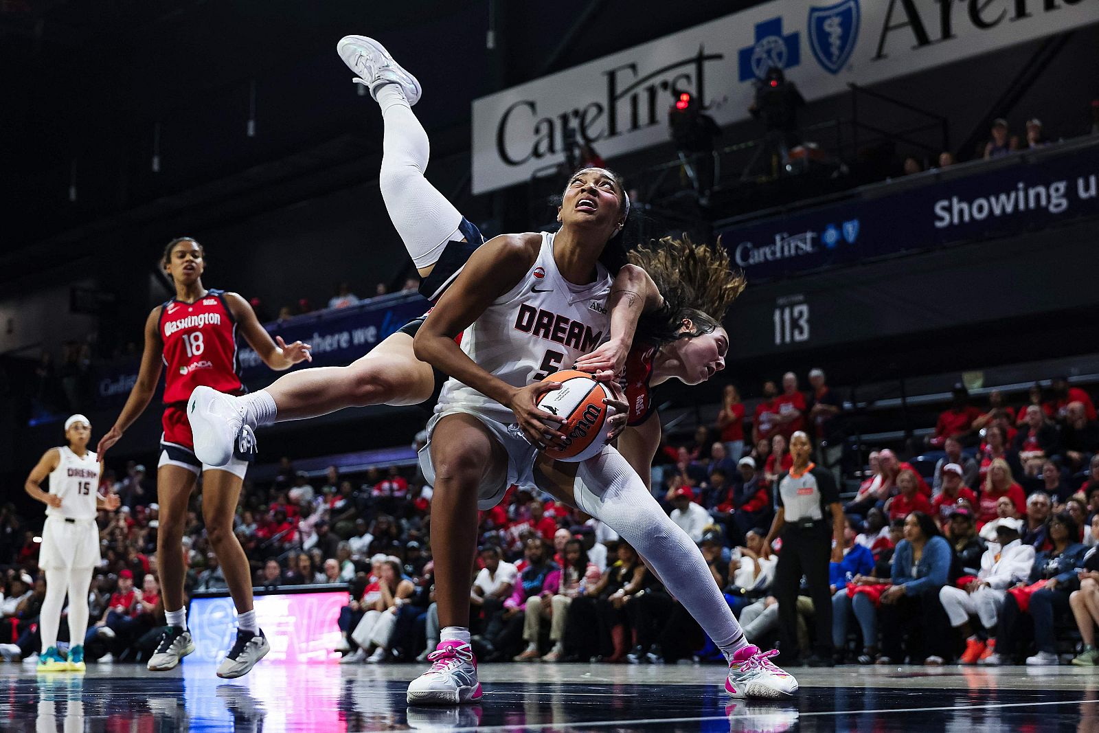 Rhyne Howard de las Atlanta Dream protege el balón mientras una jugadora de las Washington Mystics cae de forma acrobática sobre ella durante un partido de baloncesto de la WNBA.