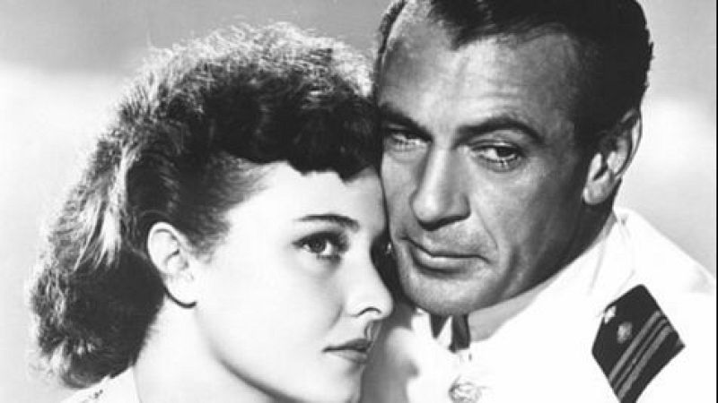 Gary Cooper, con uniforme militar, y Laraine Day posan con las mejillas juntas y expresiones serias en un retrato en blanco y negro para la película "Por el valle de las sombras".