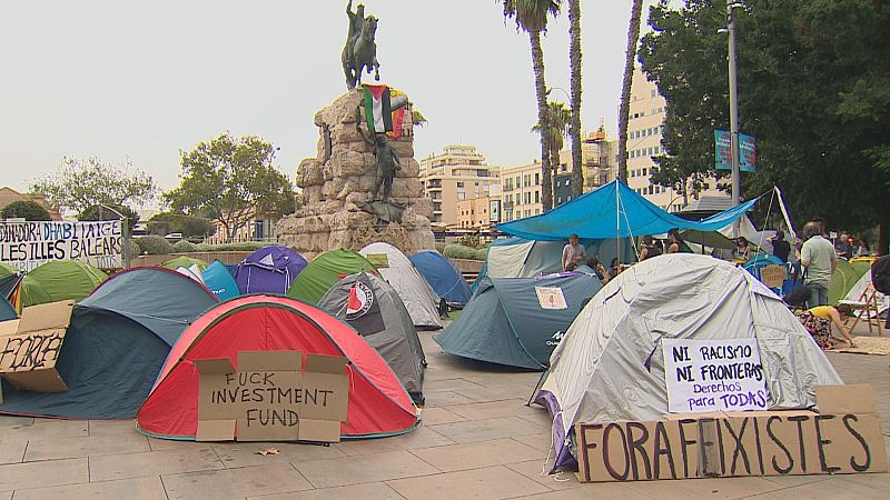 Campamento de protesta en Palma de Mallorca con tiendas de campaña y carteles como 'FUCK INVESTMENT FUND' y 'FORA FEIXISTES' ante el monumento al Rey Jaume I.