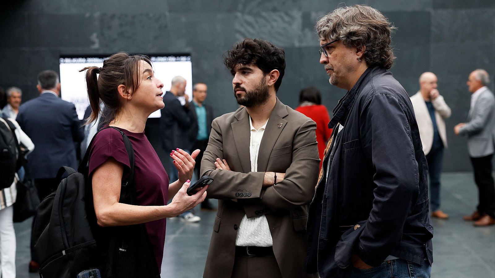 Laura Aznal, Mikel Zabaleta y Txomin González, de EH Bildu, conversan en el Parlamento de Navarra mientras ella gesticula con un móvil y ellos la escuchan con atención.