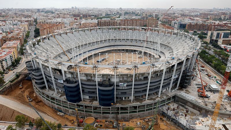Vista aérea de las obras del estadio Nou Mestalla en Valencia, destacando su estructura de hormigón vacía y torres azules con el logotipo de la constructora FCC.