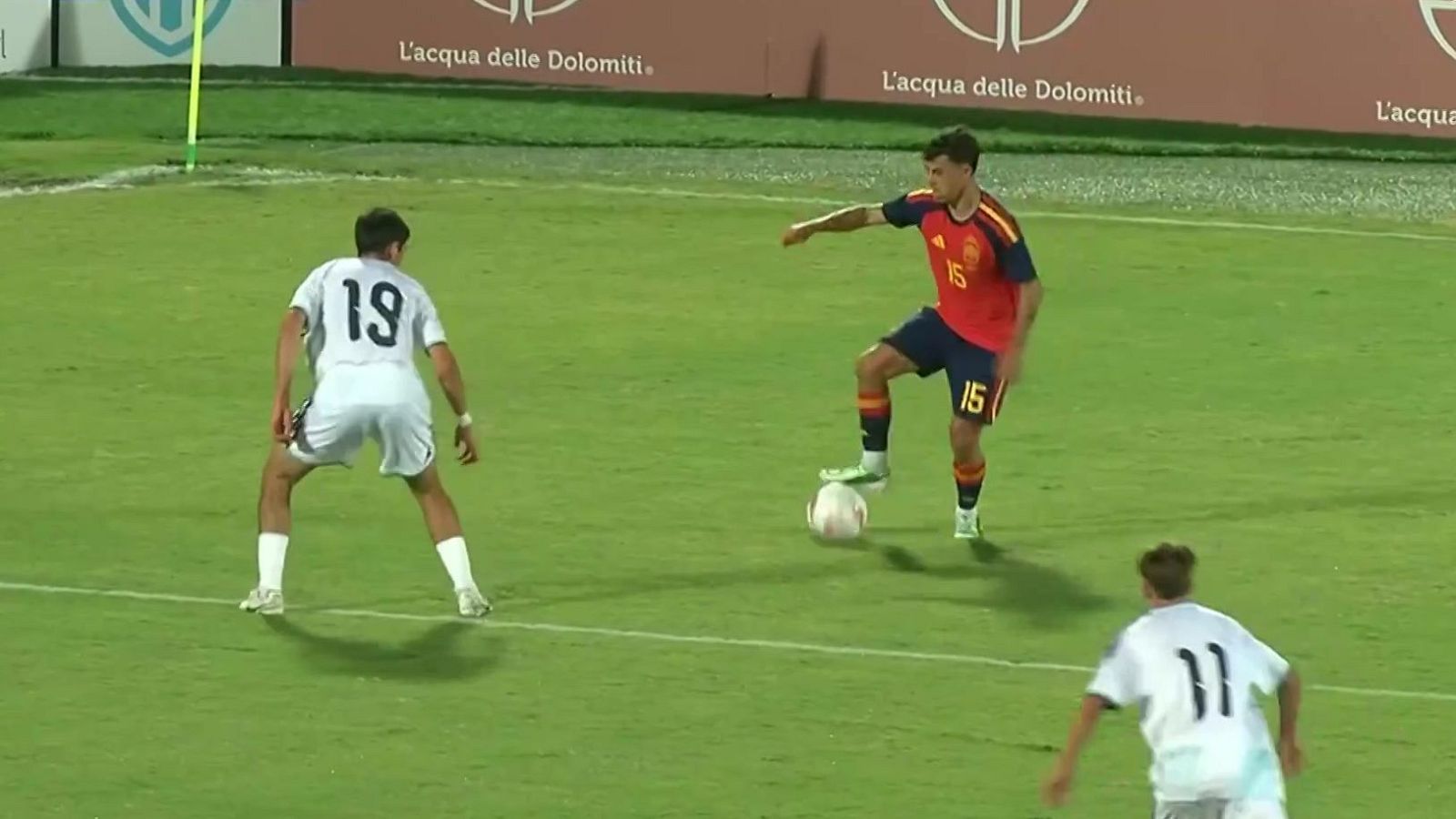 Jugador de fútbol con equipación roja y número 15 controla el balón en el campo, presionado por rivales de blanco.