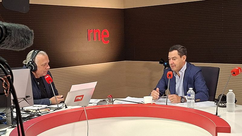 El presidente andaluz Juanma Moreno sonríe durante una entrevista radiofónica con el periodista Juan Ramón Lucas en un estudio de RNE.