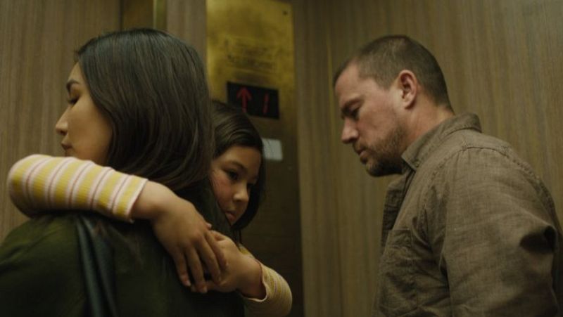 Channing Tatum, Nicole LaLiberte y Aiyana White en un ascensor. La mujer y la niña se abrazan mientras Tatum las observa con seriedad. El ascensor se mueve hacia arriba.