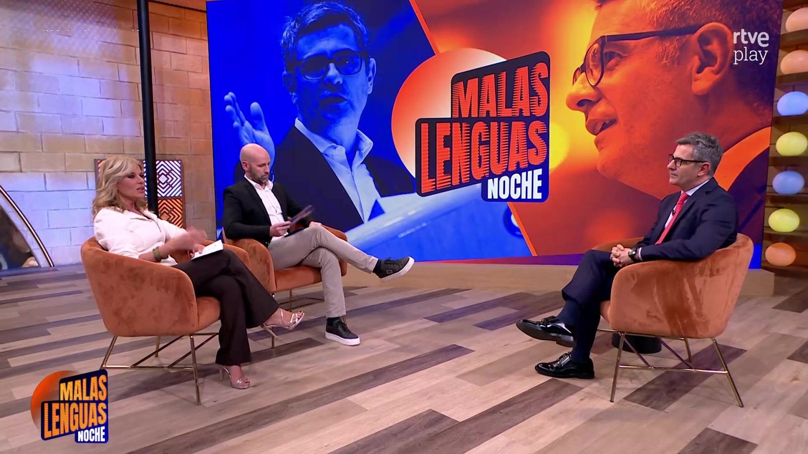 Plató de televisión con un político sentado en una butaca frente a dos periodistas y una gran pantalla de fondo.