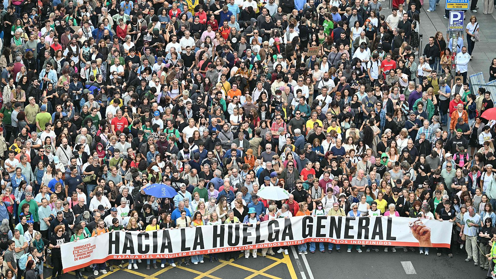 Manifestación multitudinaria en una calle urbana con una gran pancarta en primer plano que reclama bajada de alquiler y contratos indefinidos.