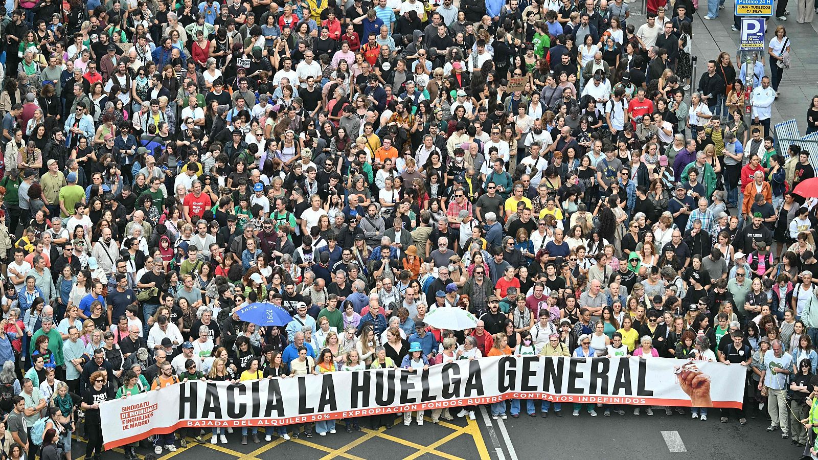 Manifestación multitudinaria en una calle urbana con una gran pancarta que pide la huelga general y la bajada de alquileres.