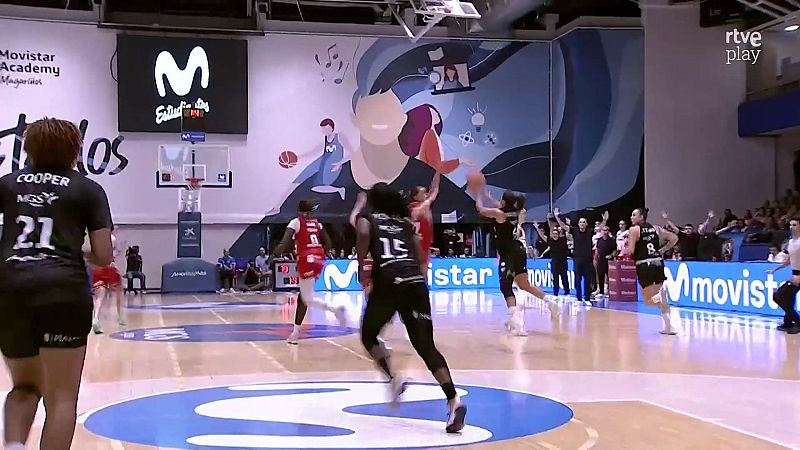 Jugadoras de baloncesto femenino disputan un partido en un pabellón, con una jugadora atacando el aro y rivales defendiendo.
